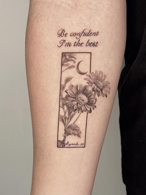 framed chrysanthemum and lettering tattoo on the forearm