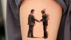 two figures shaking hands tattoo on the upper arm