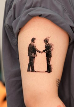 two figures shaking hands tattoo on the upper arm