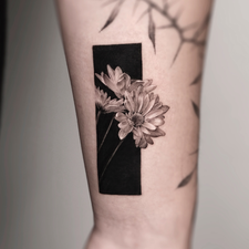flower in a black frame tattoo on the forearm