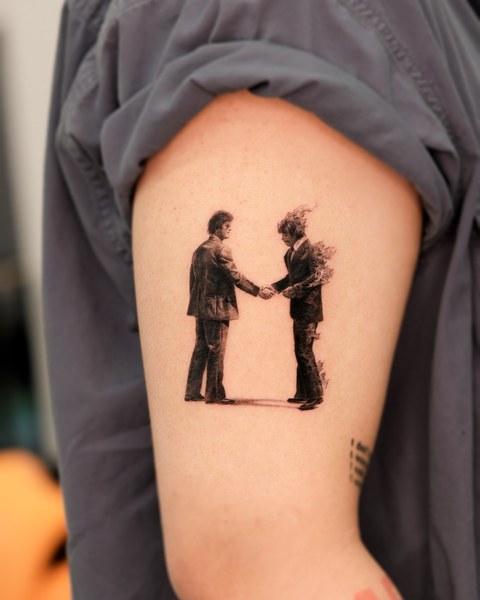 two figures shaking hands tattoo on the upper arm